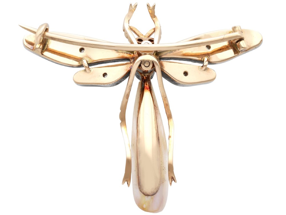 An antique late Victorian dragonfly brooch crafted in yellow gold with yellow enamel wings, garnet eyes, rose-cut diamond accents, and a elongated natural pearl abdomen. View X