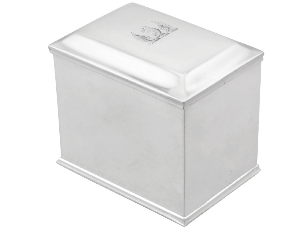 A rectangular George III sterling silver tea caddy featuring a fitted cover engraved with a heraldic crest and stepped moulded borders along the base and top.