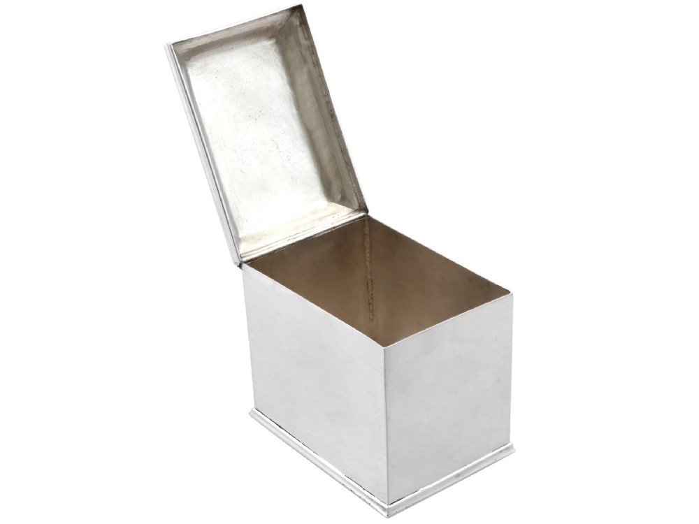 A rectangular George III sterling silver tea caddy featuring a fitted cover engraved with a heraldic crest and stepped moulded borders along the base and top. View VI