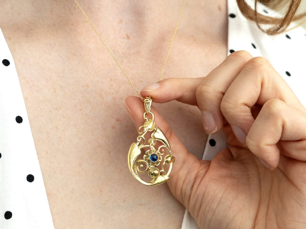 An openwork Art Nouveau 14ct yellow gold pendant featuring botanical leaf motifs surrounding a central bezel-set blue sapphire. View IV