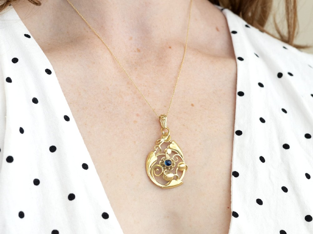 An openwork Art Nouveau 14ct yellow gold pendant featuring botanical leaf motifs surrounding a central bezel-set blue sapphire. View V