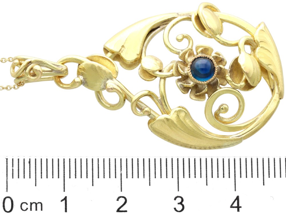 An openwork Art Nouveau 14ct yellow gold pendant featuring botanical leaf motifs surrounding a central bezel-set blue sapphire. View IX