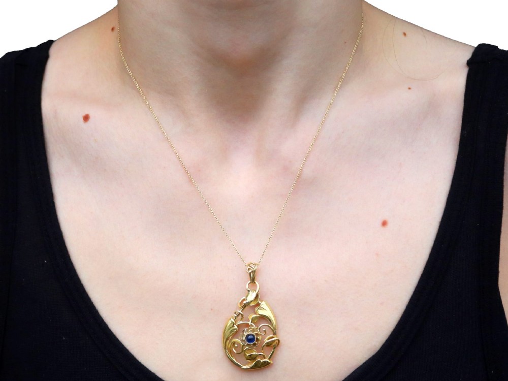 An openwork Art Nouveau 14ct yellow gold pendant featuring botanical leaf motifs surrounding a central bezel-set blue sapphire. View XI