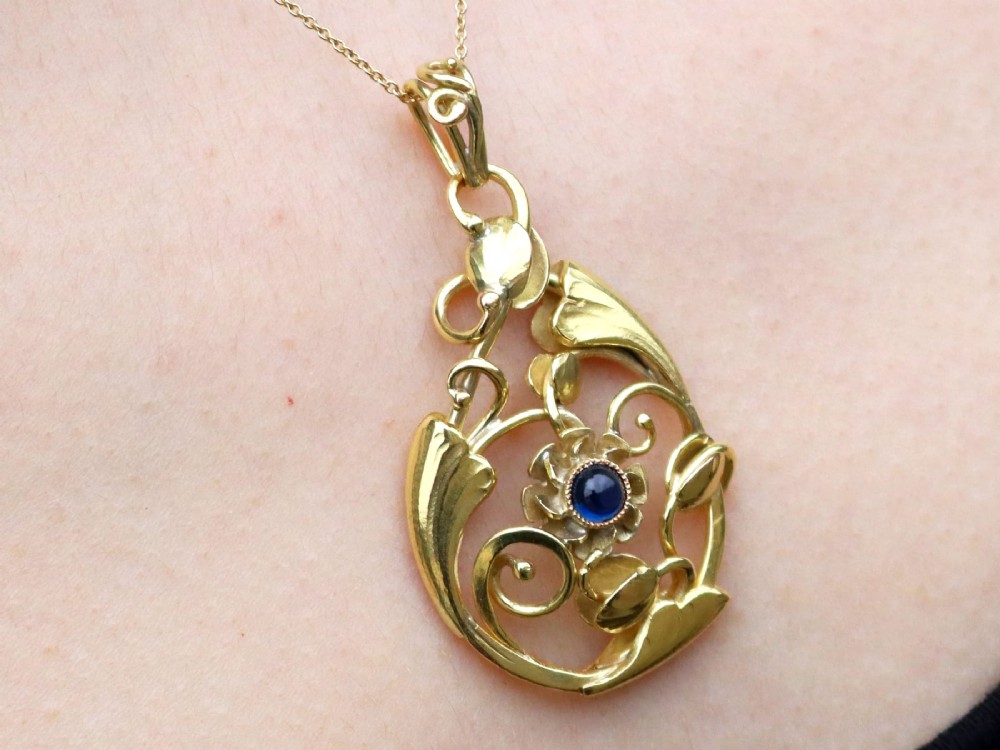 An openwork Art Nouveau 14ct yellow gold pendant featuring botanical leaf motifs surrounding a central bezel-set blue sapphire. View XII