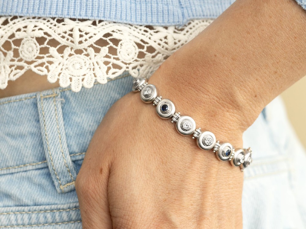 A vintage 18ct white gold articulated link bracelet set with alternating bezel-mounted round diamonds and blue sapphires. View V