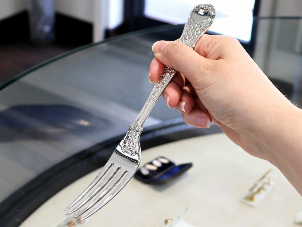 A collection of ornate sterling silver cutlery pieces featuring intricately embossed handles and polished bowls, including ladles, forks, knives, and spoons. View IV