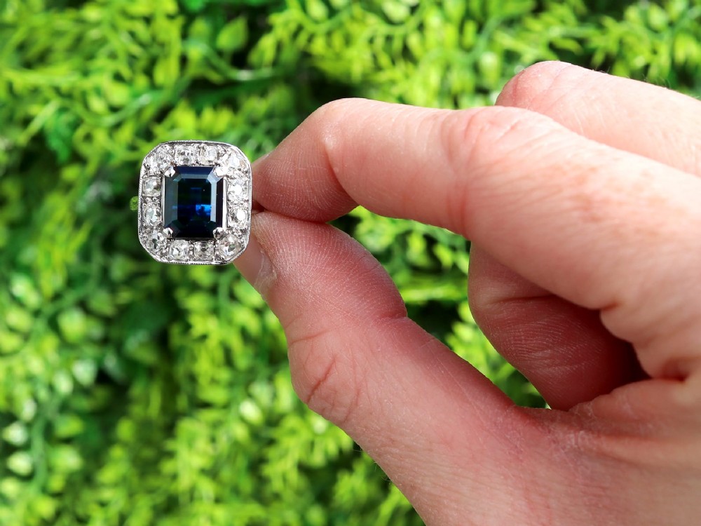 An Art Deco platinum cluster ring featuring a central rectangular blue sapphire surrounded by twelve old-cut diamonds with millegrain edges. View II