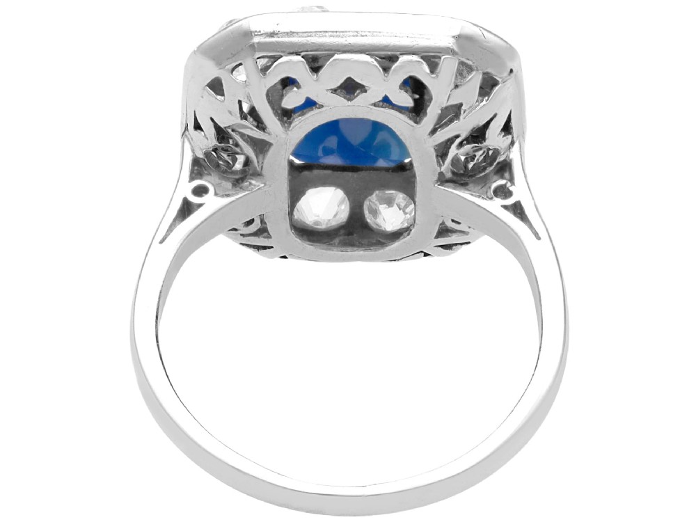 An Art Deco platinum cluster ring featuring a central rectangular blue sapphire surrounded by twelve old-cut diamonds with millegrain edges. View VIII