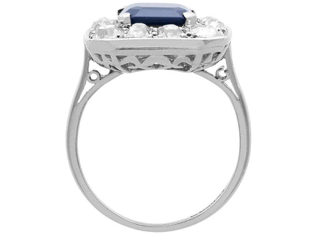 An Art Deco platinum cluster ring featuring a central rectangular blue sapphire surrounded by twelve old-cut diamonds with millegrain edges. View IX