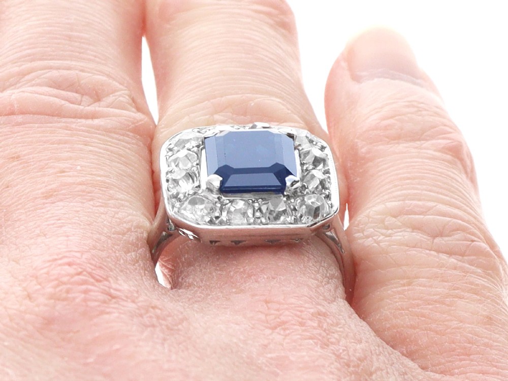 An Art Deco platinum cluster ring featuring a central rectangular blue sapphire surrounded by twelve old-cut diamonds with millegrain edges. View XII