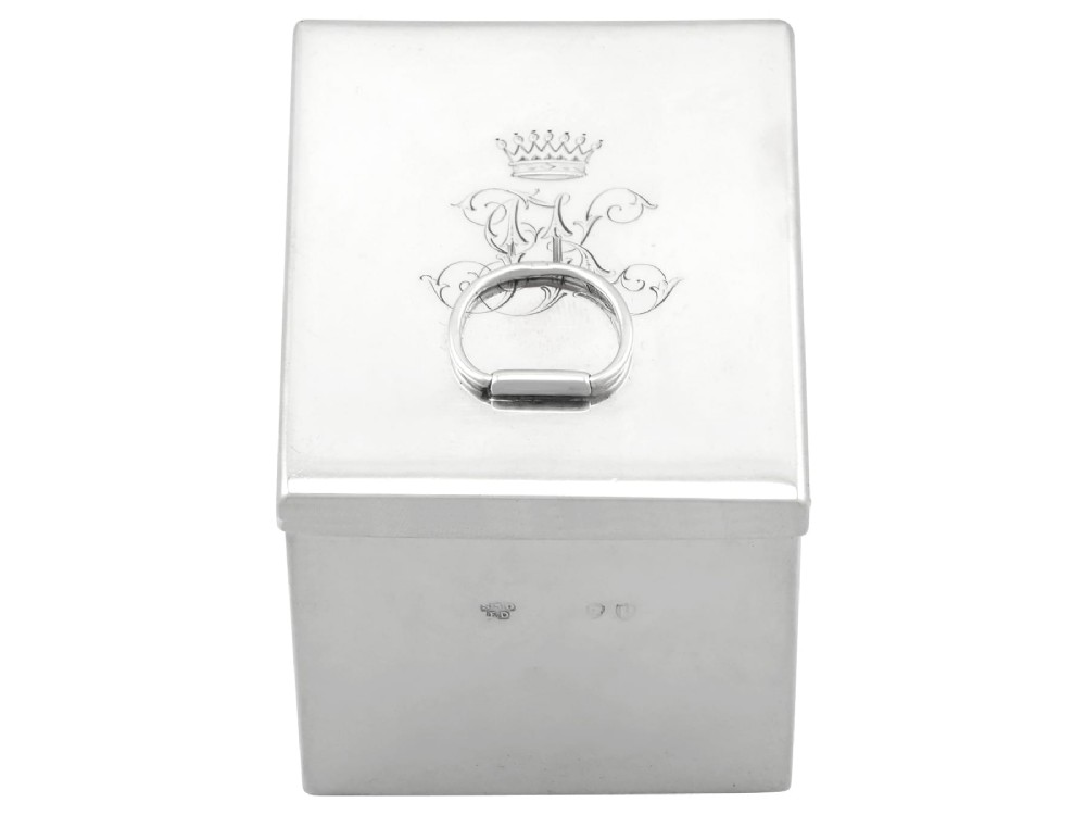 A rectangular Victorian sterling silver tea caddy featuring an engraved crest, top folding handle, and visible side hallmarks. View IV