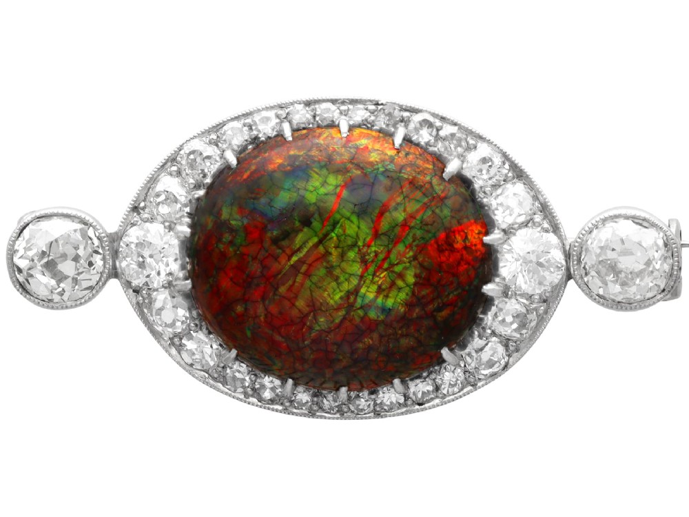 An Edwardian platinum brooch featuring an oval cabochon boulder opal surrounded by a halo of diamonds and two outer accent diamonds.
