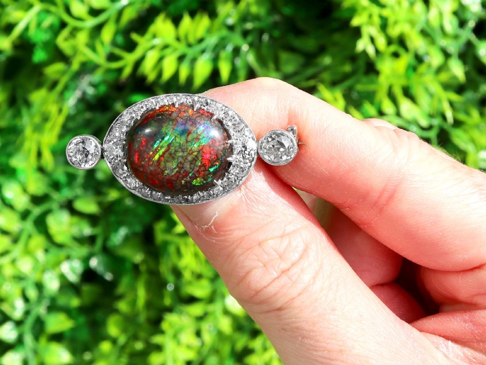 An Edwardian platinum brooch featuring an oval cabochon boulder opal surrounded by a halo of diamonds and two outer accent diamonds. View II