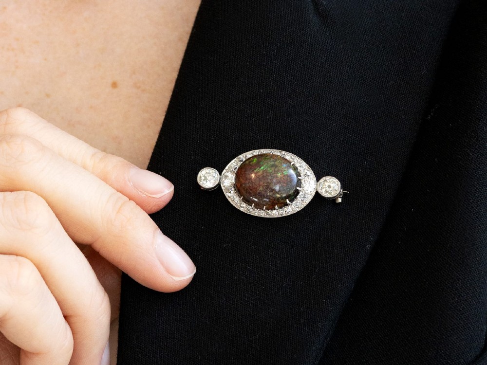 An Edwardian platinum brooch featuring an oval cabochon boulder opal surrounded by a halo of diamonds and two outer accent diamonds. View III