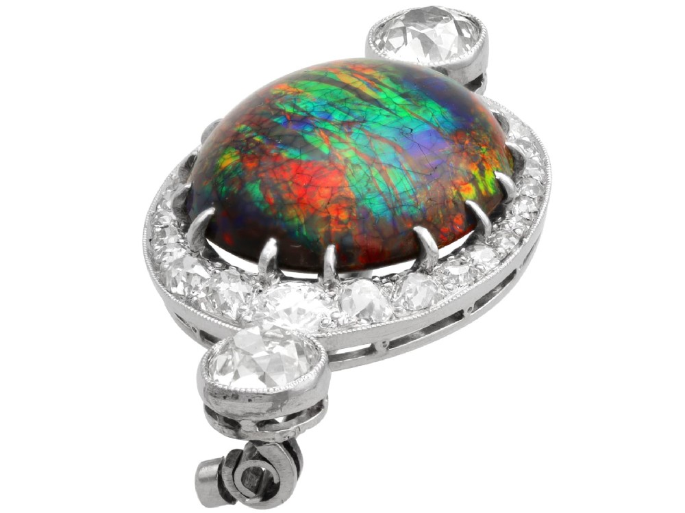 An Edwardian platinum brooch featuring an oval cabochon boulder opal surrounded by a halo of diamonds and two outer accent diamonds. View VI