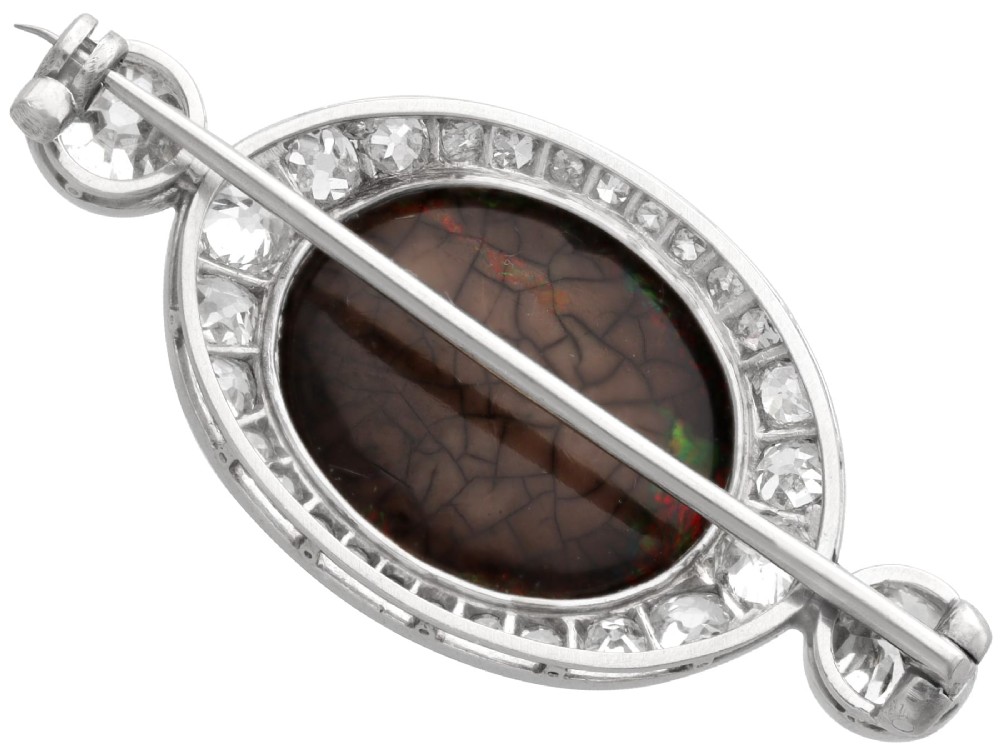 An Edwardian platinum brooch featuring an oval cabochon boulder opal surrounded by a halo of diamonds and two outer accent diamonds. View VII