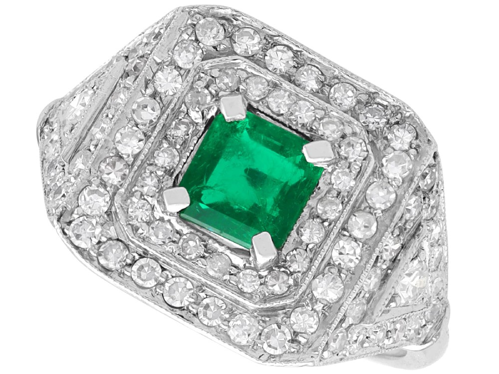 An Art Deco platinum ring featuring a central square green emerald surrounded by geometric concentric halos of brilliant-cut diamonds.