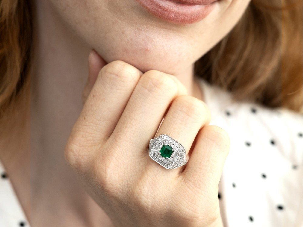An Art Deco platinum ring featuring a central square green emerald surrounded by geometric concentric halos of brilliant-cut diamonds. View III