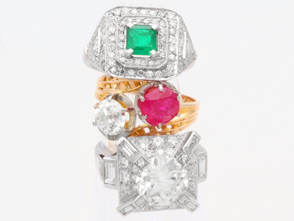 An Art Deco platinum ring featuring a central square green emerald surrounded by geometric concentric halos of brilliant-cut diamonds. View IV