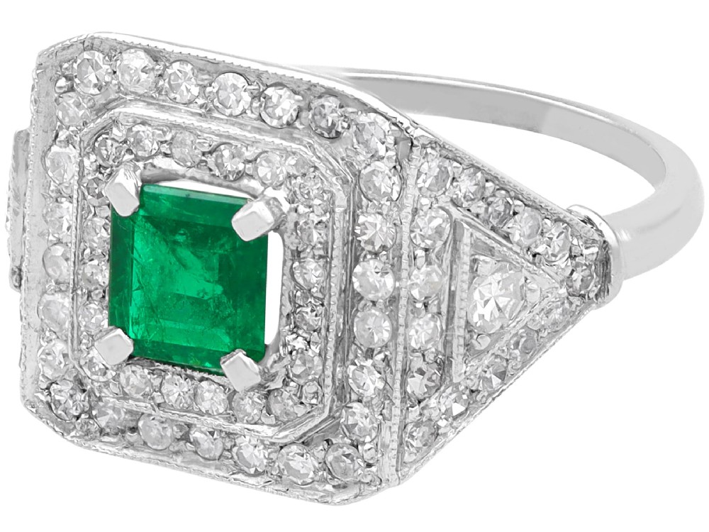 An Art Deco platinum ring featuring a central square green emerald surrounded by geometric concentric halos of brilliant-cut diamonds. View V