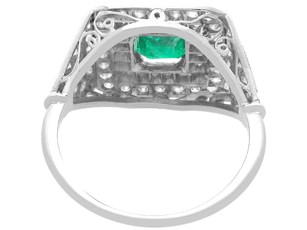 An Art Deco platinum ring featuring a central square green emerald surrounded by geometric concentric halos of brilliant-cut diamonds. View VI
