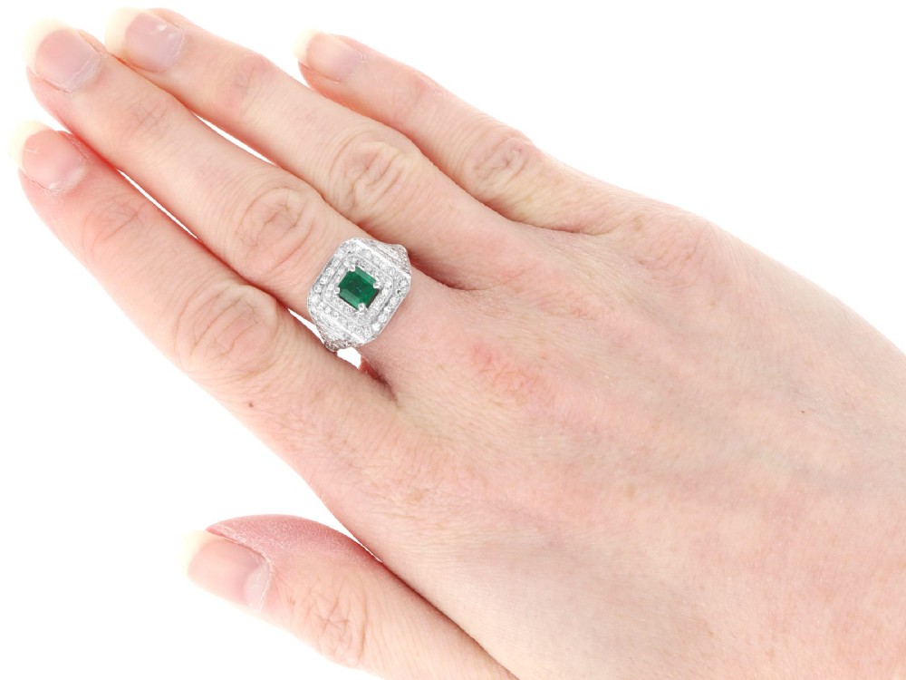 An Art Deco platinum ring featuring a central square green emerald surrounded by geometric concentric halos of brilliant-cut diamonds. View VIII