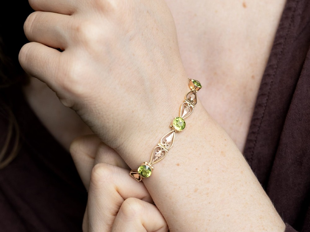 An antique Art Nouveau 9ct yellow gold bracelet featuring round-cut green peridots held in collet settings between openwork scroll links. View IV