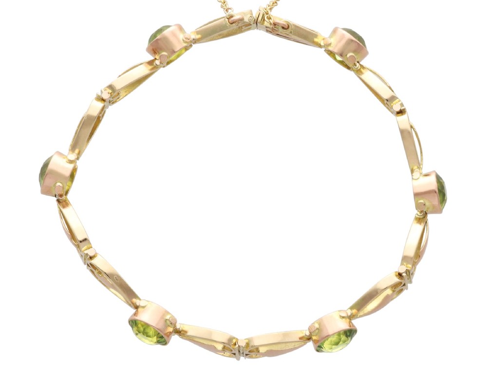 An antique Art Nouveau 9ct yellow gold bracelet featuring round-cut green peridots held in collet settings between openwork scroll links. View VI