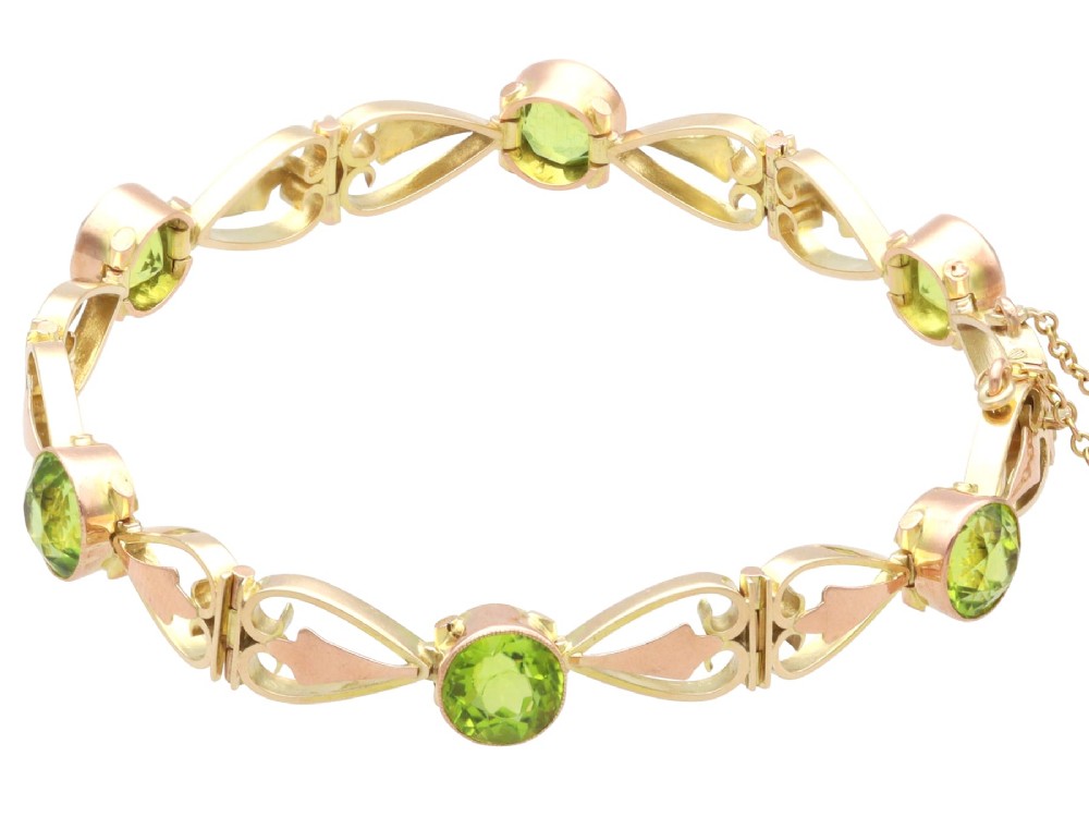 An antique Art Nouveau 9ct yellow gold bracelet featuring round-cut green peridots held in collet settings between openwork scroll links. View VII