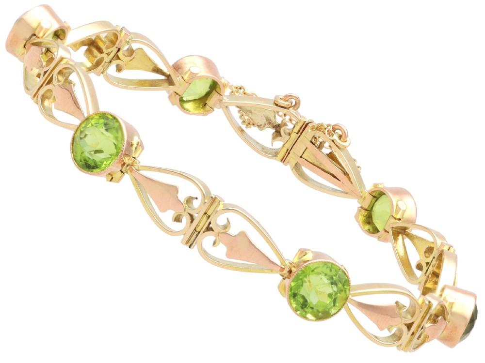 An antique Art Nouveau 9ct yellow gold bracelet featuring round-cut green peridots held in collet settings between openwork scroll links. View VIII