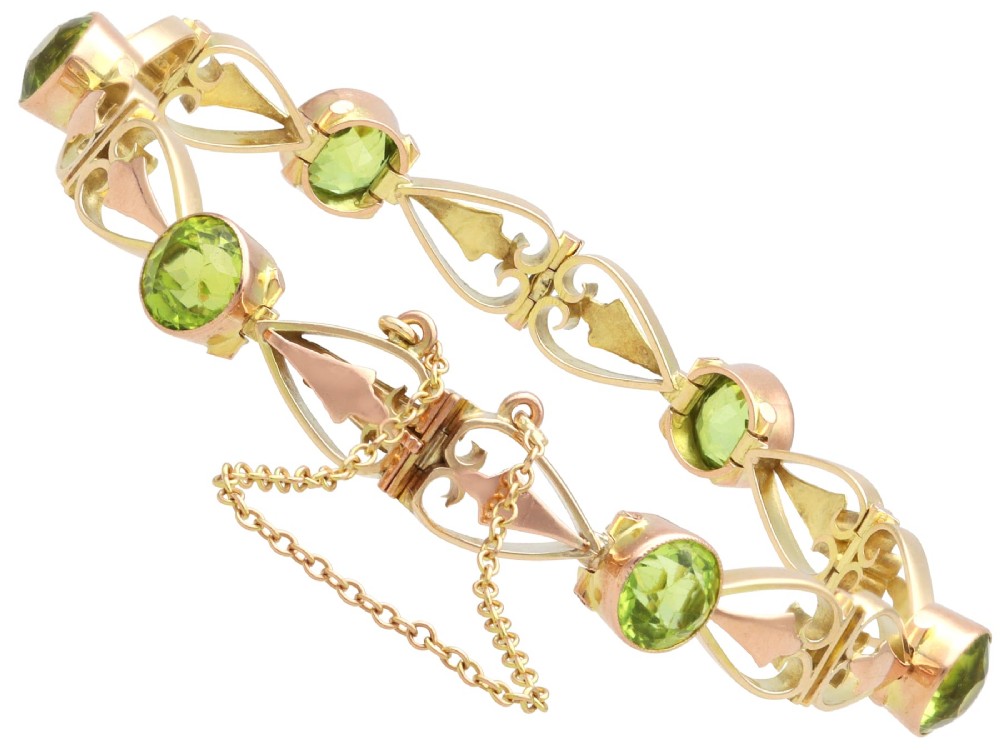 An antique Art Nouveau 9ct yellow gold bracelet featuring round-cut green peridots held in collet settings between openwork scroll links. View IX