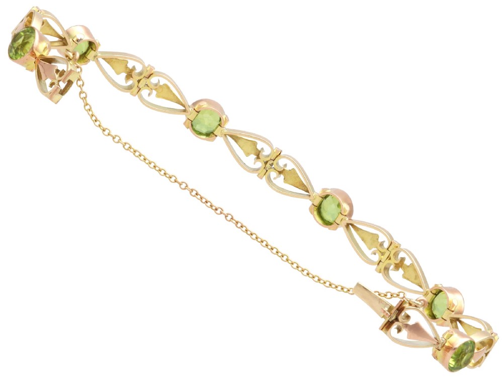An antique Art Nouveau 9ct yellow gold bracelet featuring round-cut green peridots held in collet settings between openwork scroll links. View X
