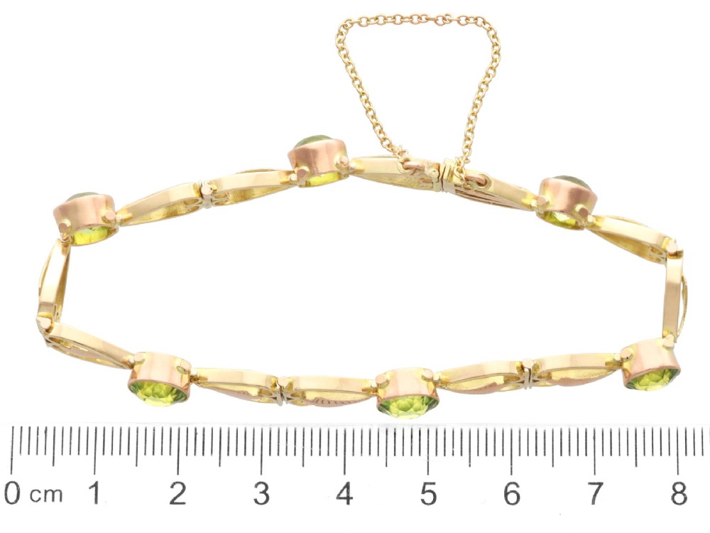 An antique Art Nouveau 9ct yellow gold bracelet featuring round-cut green peridots held in collet settings between openwork scroll links. View XI