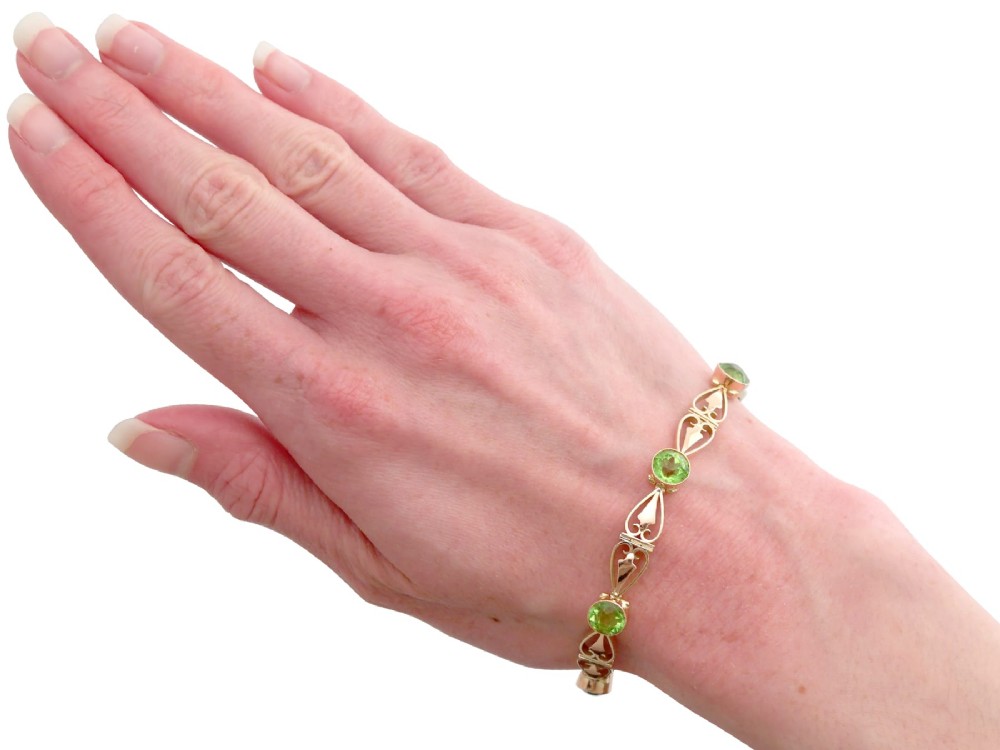 An antique Art Nouveau 9ct yellow gold bracelet featuring round-cut green peridots held in collet settings between openwork scroll links. View XIII