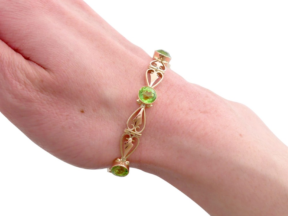 An antique Art Nouveau 9ct yellow gold bracelet featuring round-cut green peridots held in collet settings between openwork scroll links. View XIV