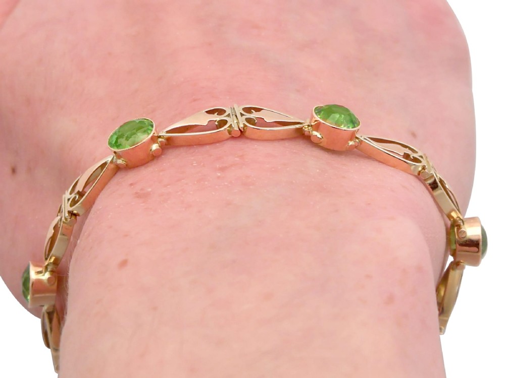 An antique Art Nouveau 9ct yellow gold bracelet featuring round-cut green peridots held in collet settings between openwork scroll links. View XV