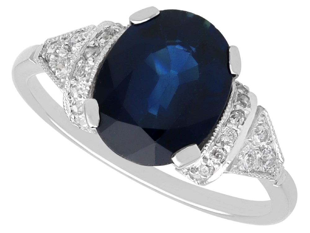 An Art Deco platinum ring featuring a centrally set oval blue sapphire flanked by diamond-set geometric shoulders.