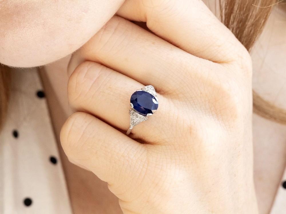 An Art Deco platinum ring featuring a centrally set oval blue sapphire flanked by diamond-set geometric shoulders. View III