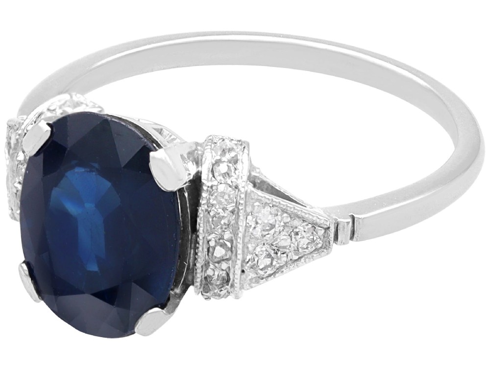 An Art Deco platinum ring featuring a centrally set oval blue sapphire flanked by diamond-set geometric shoulders. View IV