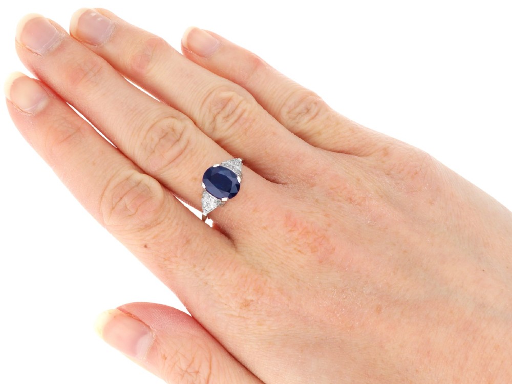 An Art Deco platinum ring featuring a centrally set oval blue sapphire flanked by diamond-set geometric shoulders. View VIII