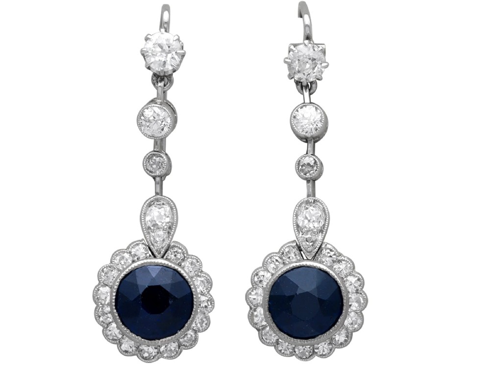 A pair of antique Art Deco platinum drop earrings featuring round dark blue sapphires encircled by diamond halos suspended from articulated diamond links.