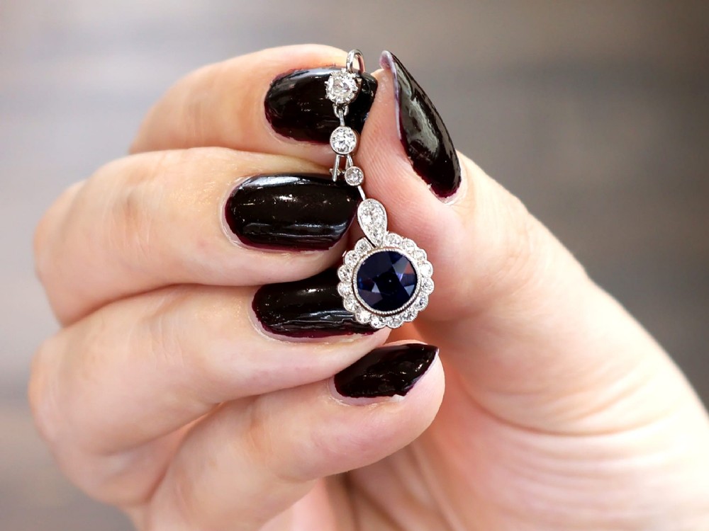A pair of antique Art Deco platinum drop earrings featuring round dark blue sapphires encircled by diamond halos suspended from articulated diamond links. View III