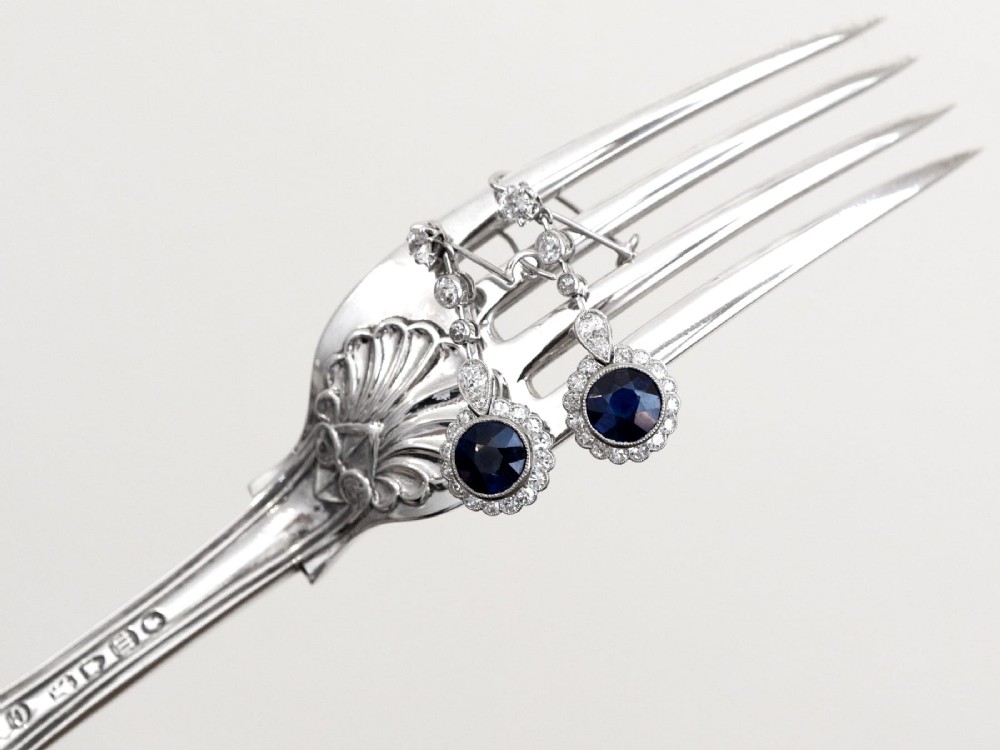 A pair of antique Art Deco platinum drop earrings featuring round dark blue sapphires encircled by diamond halos suspended from articulated diamond links. View VI