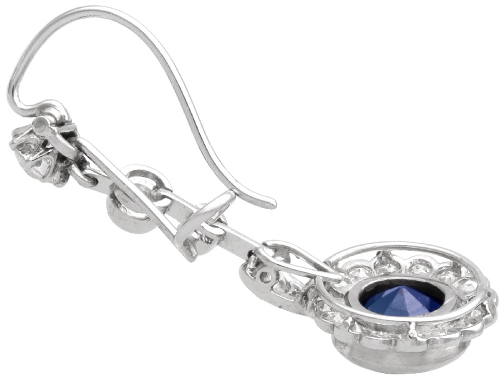 A pair of antique Art Deco platinum drop earrings featuring round dark blue sapphires encircled by diamond halos suspended from articulated diamond links. View VII