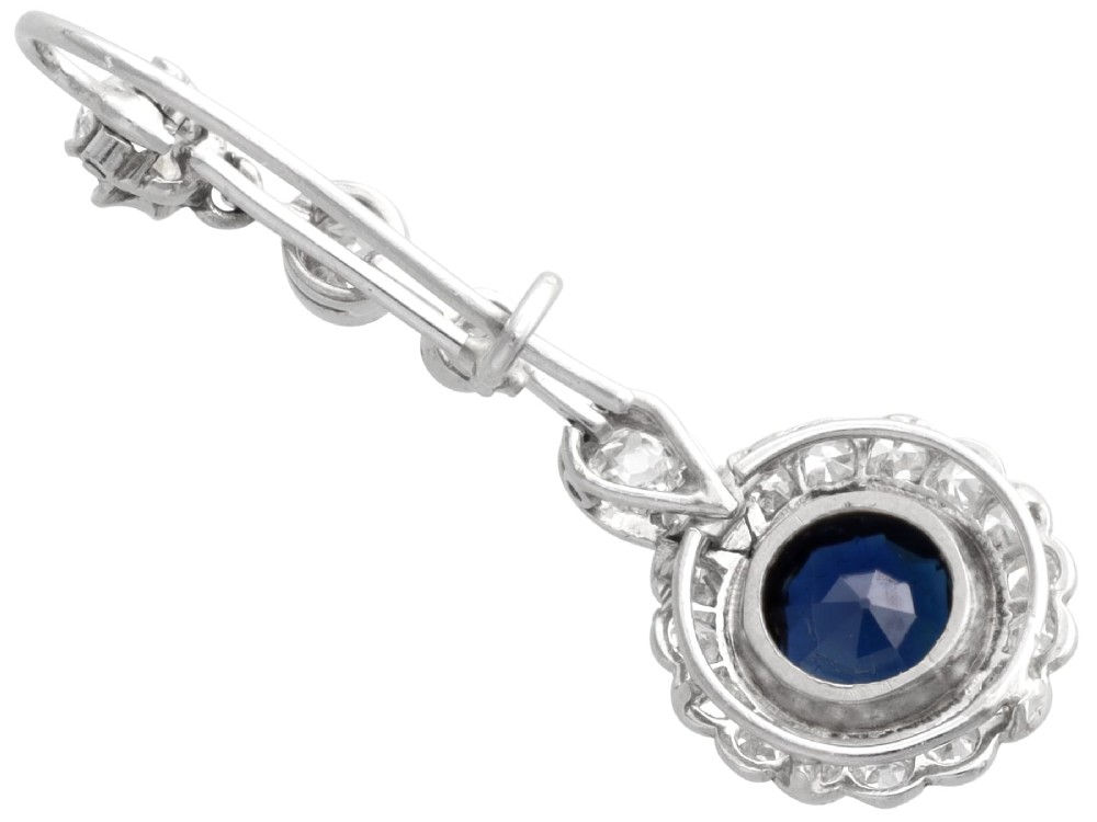 A pair of antique Art Deco platinum drop earrings featuring round dark blue sapphires encircled by diamond halos suspended from articulated diamond links. View VIII