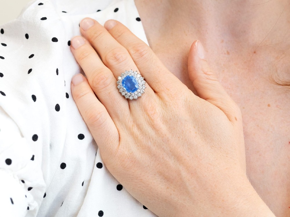 A vintage 14ct white gold cluster ring featuring a centrally mounted cushion-cut blue Ceylon sapphire surrounded by a double halo of round brilliant diamonds. View V