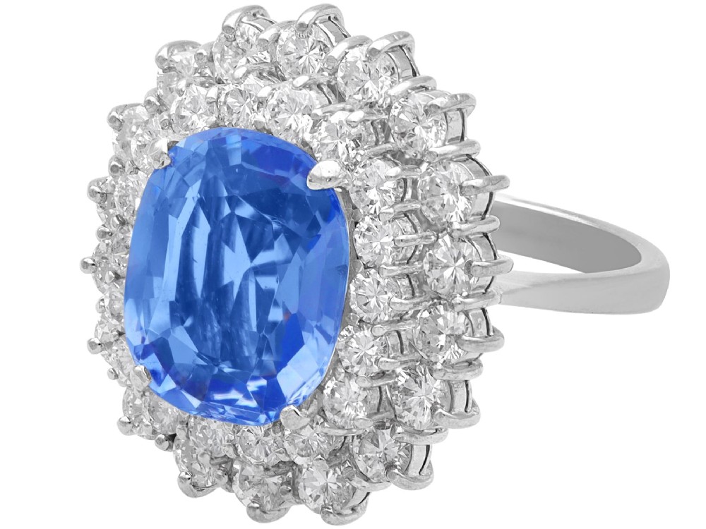 A vintage 14ct white gold cluster ring featuring a centrally mounted cushion-cut blue Ceylon sapphire surrounded by a double halo of round brilliant diamonds. View VI