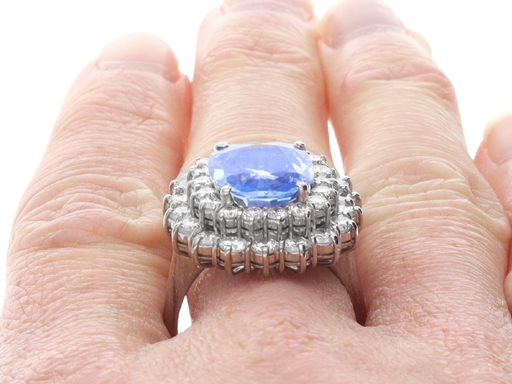 A vintage 14ct white gold cluster ring featuring a centrally mounted cushion-cut blue Ceylon sapphire surrounded by a double halo of round brilliant diamonds. View XI