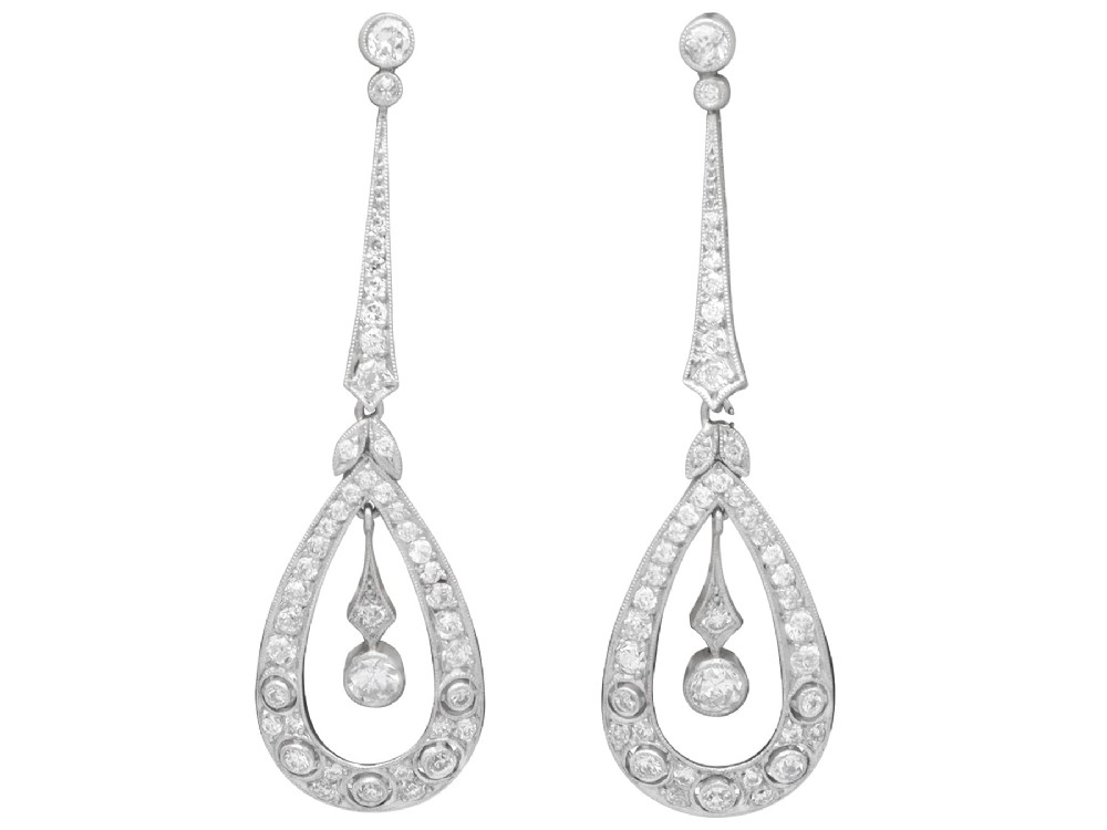 A pair of Art Deco platinum drop earrings featuring openwork teardrop frames set with diamonds and geometric articulated tops.