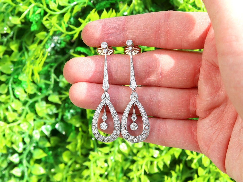 A pair of Art Deco platinum drop earrings featuring openwork teardrop frames set with diamonds and geometric articulated tops. View II